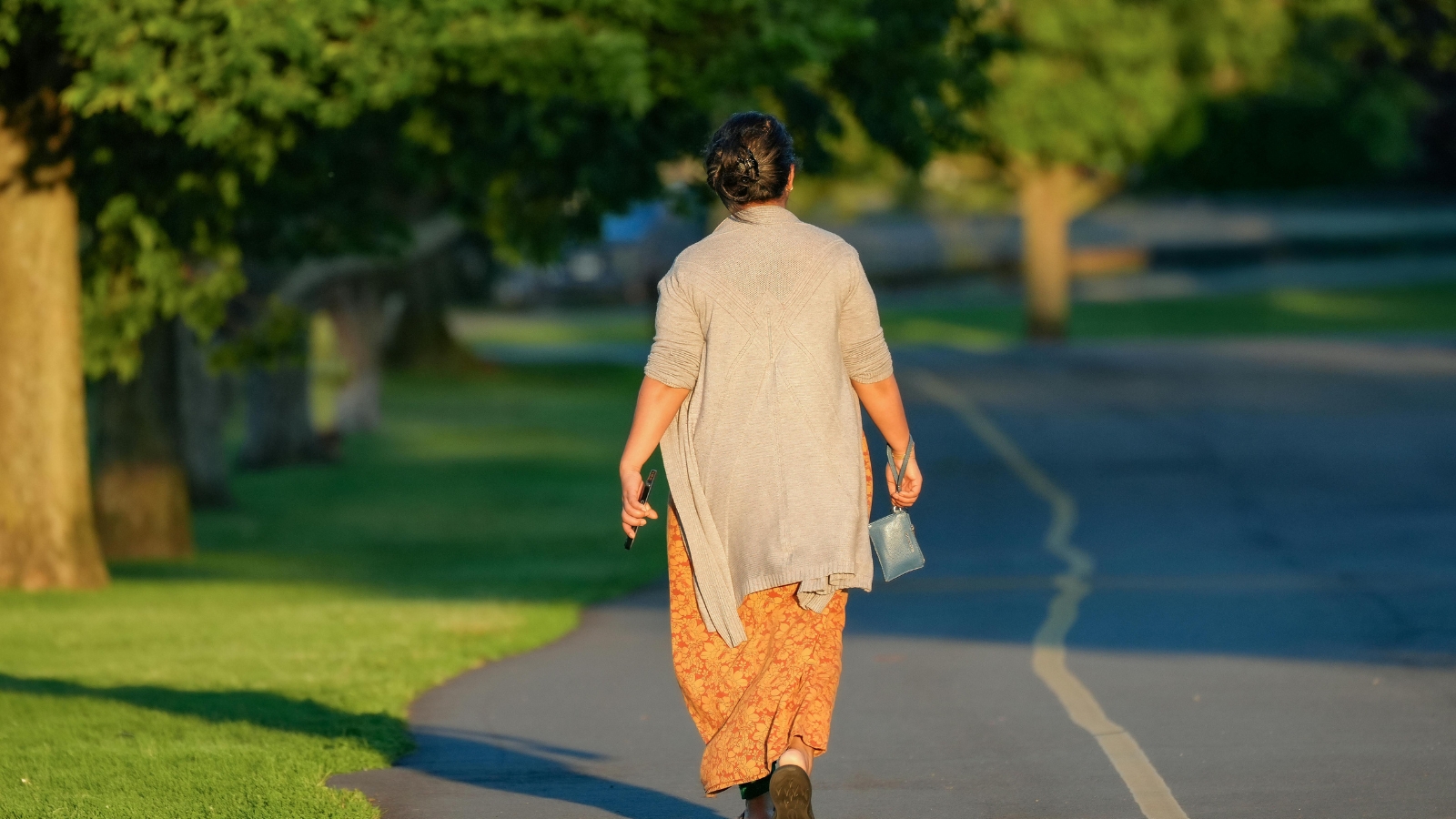 Woman walking through a sunny park on a morning walk, seen from behind.